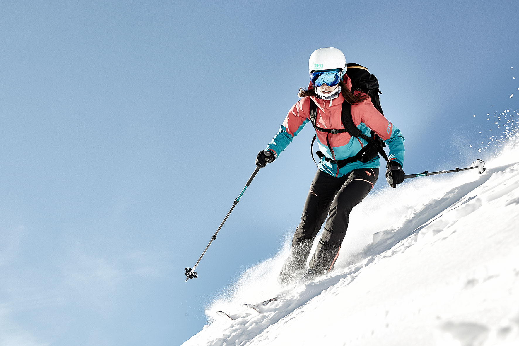 Roxy speeding down a steep mountain slope near Innsbruck, the spray behind her and against a blue sunny sky.