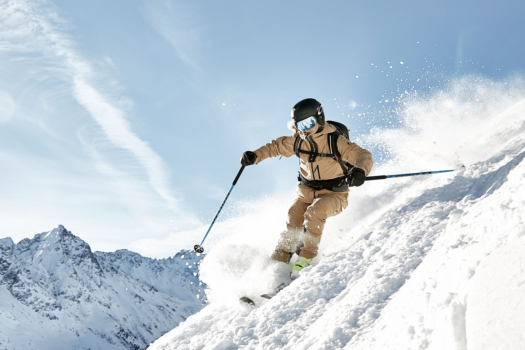 Woman skiing down a steep slope in the Alps near Innsbruck, with the snow spraying behind her and the mounains in the background