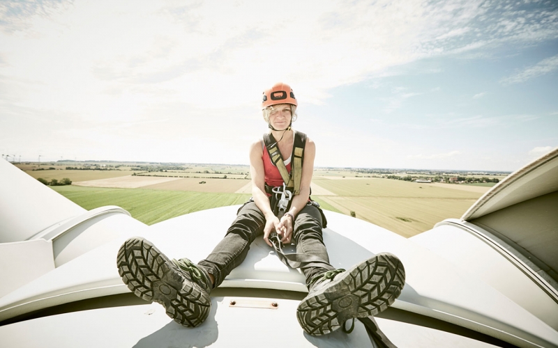 Cape Town photographer Jessica Zumpfe sitting on top of a wind turbine with a helmet and safety gear while on a shoot for a alternative energy client.