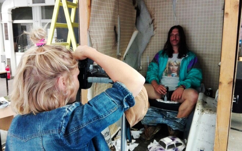 Over-the shoulder shot of Jessica Zumpfe Photography shooting a campaign for Goldeimer compost toilets, of the model sitting on the toilet, holding a beer between his legs.