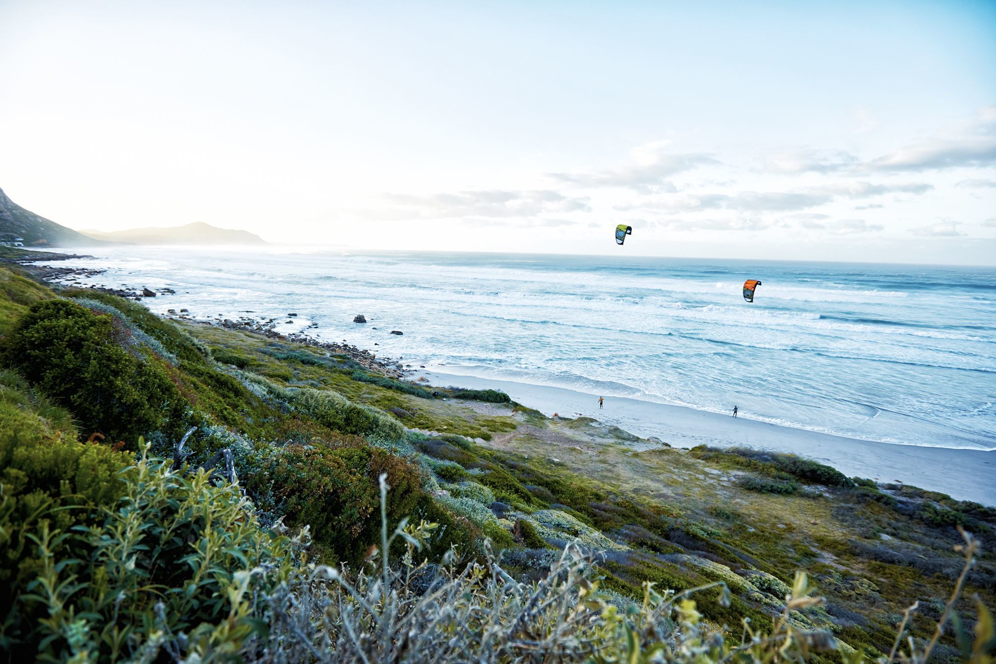 Two kiters going out into the waves at sunrise at witsands beach in cape town