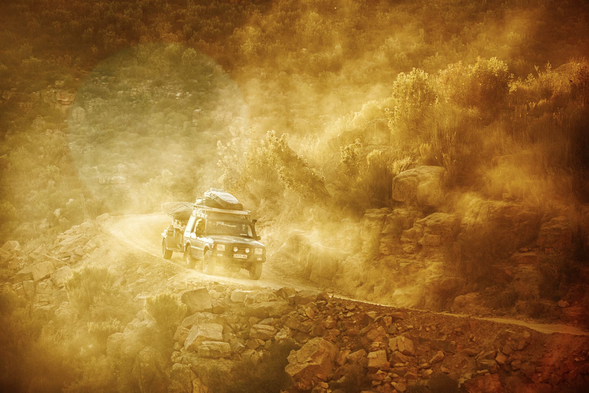 Landrover Discovery rounding a corner in the mountains on a mountain pass, kicking up the dust in he sunset.