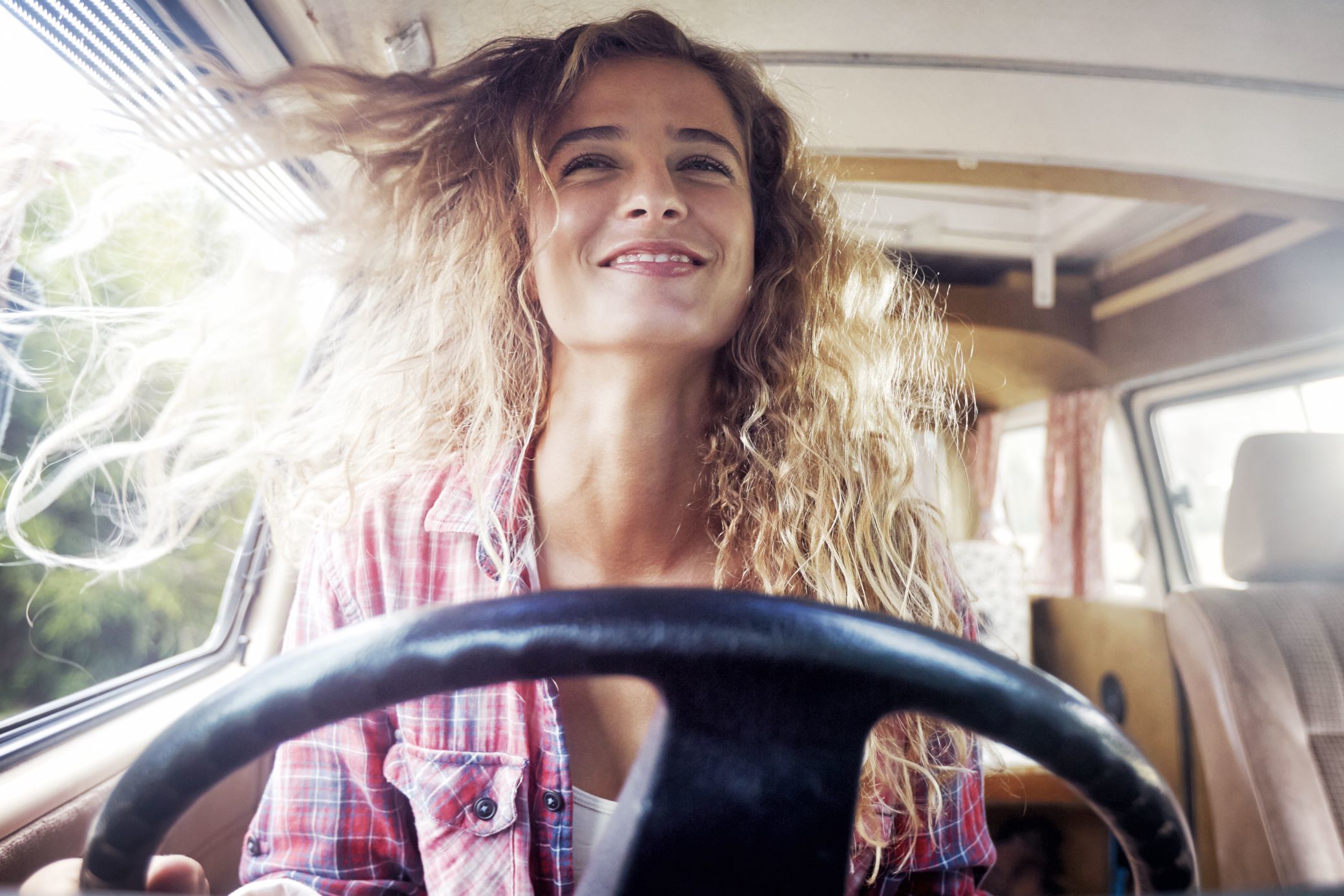 Portrait of a woman sitting at the wheel of her vw camper van smiling. Her hair is blowing in the wind. Shot as part of a self portrait story by Cape Town Photographer Jessica Zumpfe