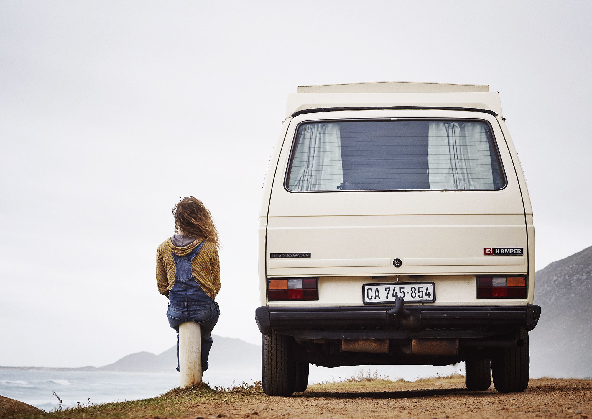 A girl sitting next to her van both enjoying the view over the ocean at misty cliffs in cape town.