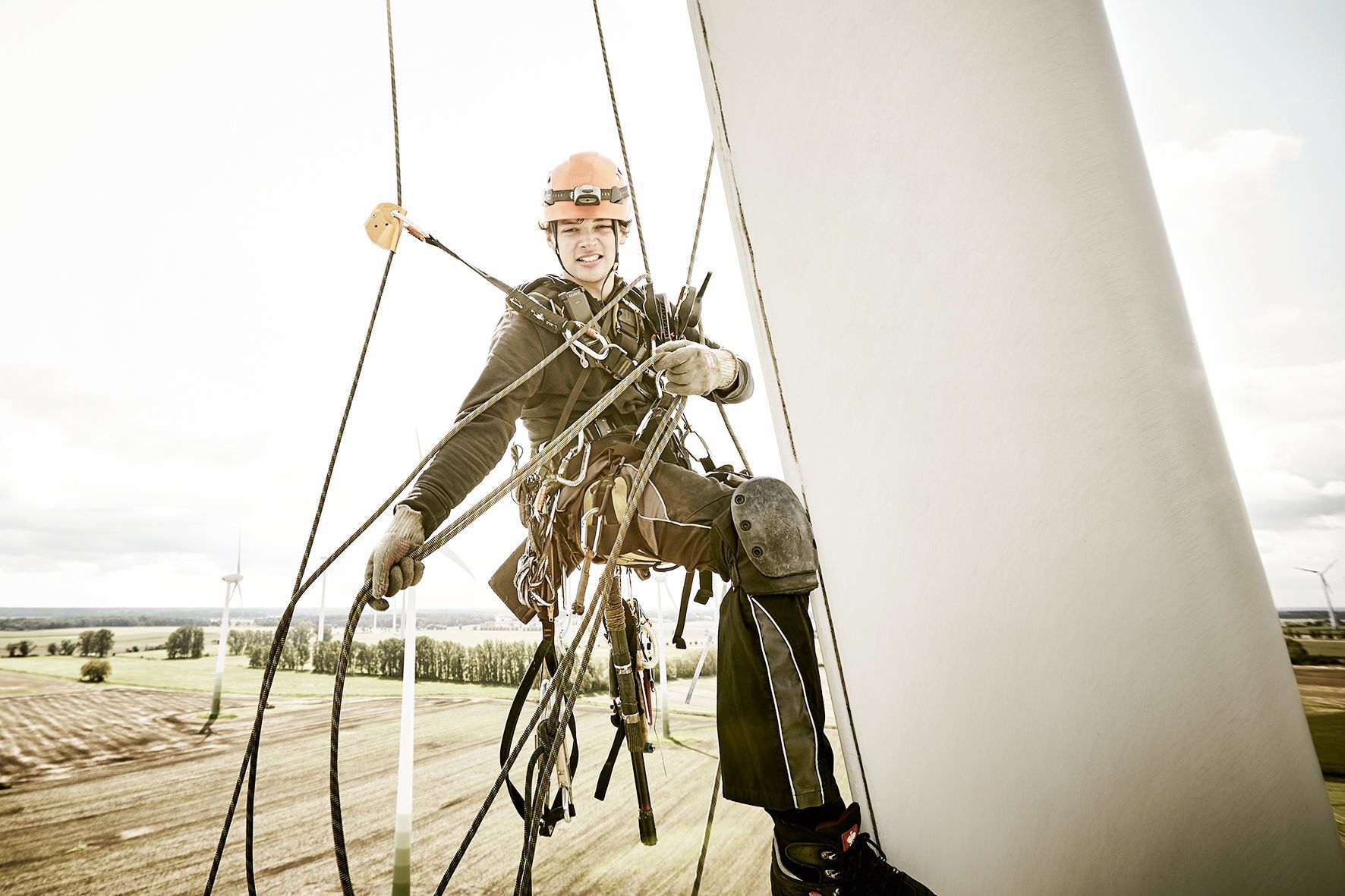 Close-up portrait of an industrial climber hanging in the ropes on a rotor blade, pulling the photographer who is hanging in the ropes beside him closer.