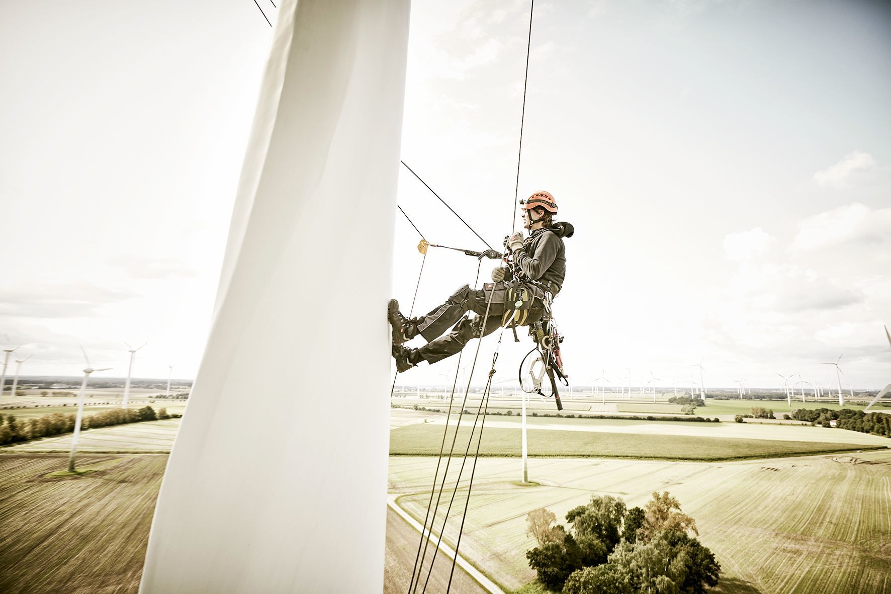 Rotor blade mechanic abseiling down a wind turbine with a view of the wind park on Fehmarn behind him.