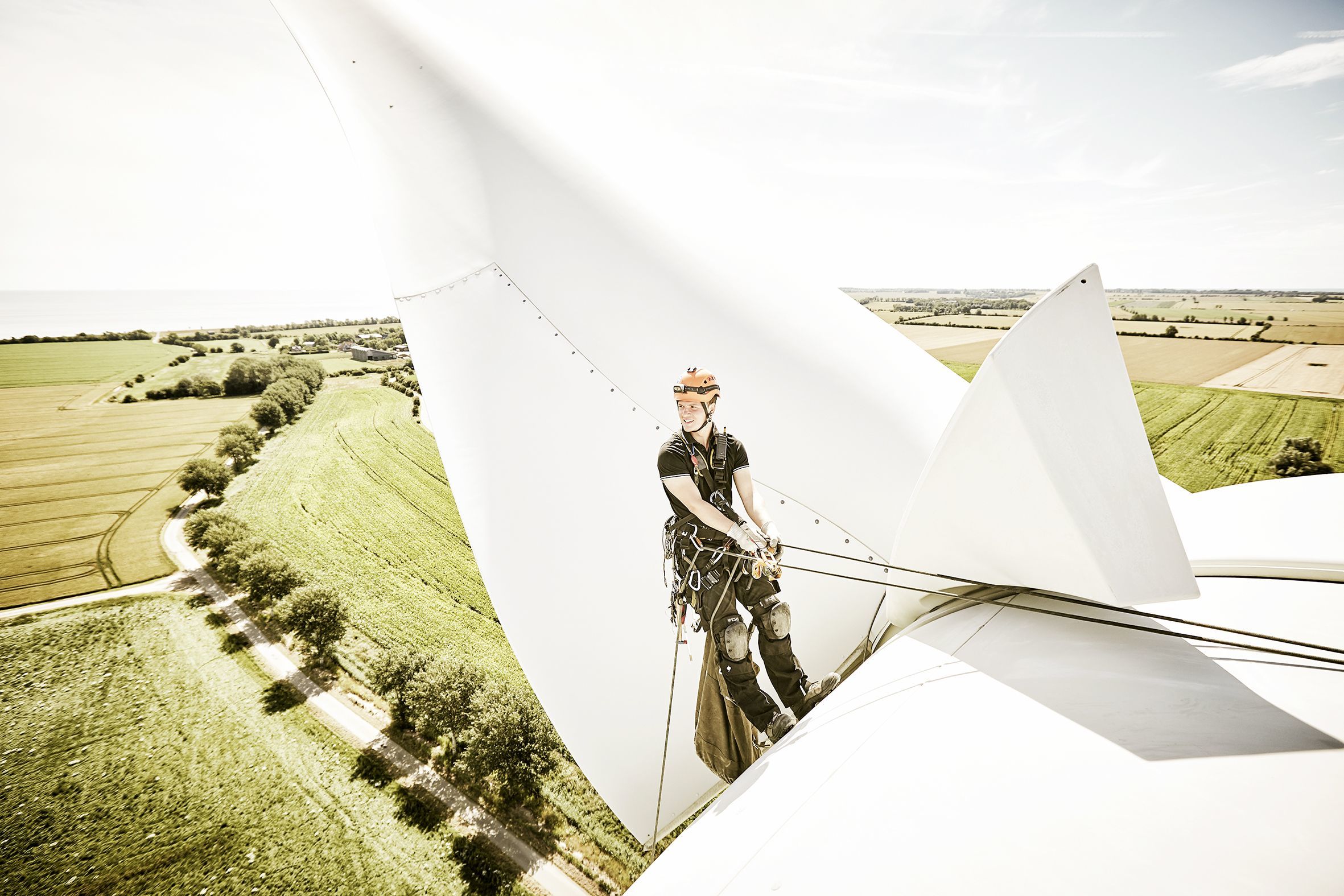 Industrial climber abseiling down a wind turbine with a magnificent view behind him.