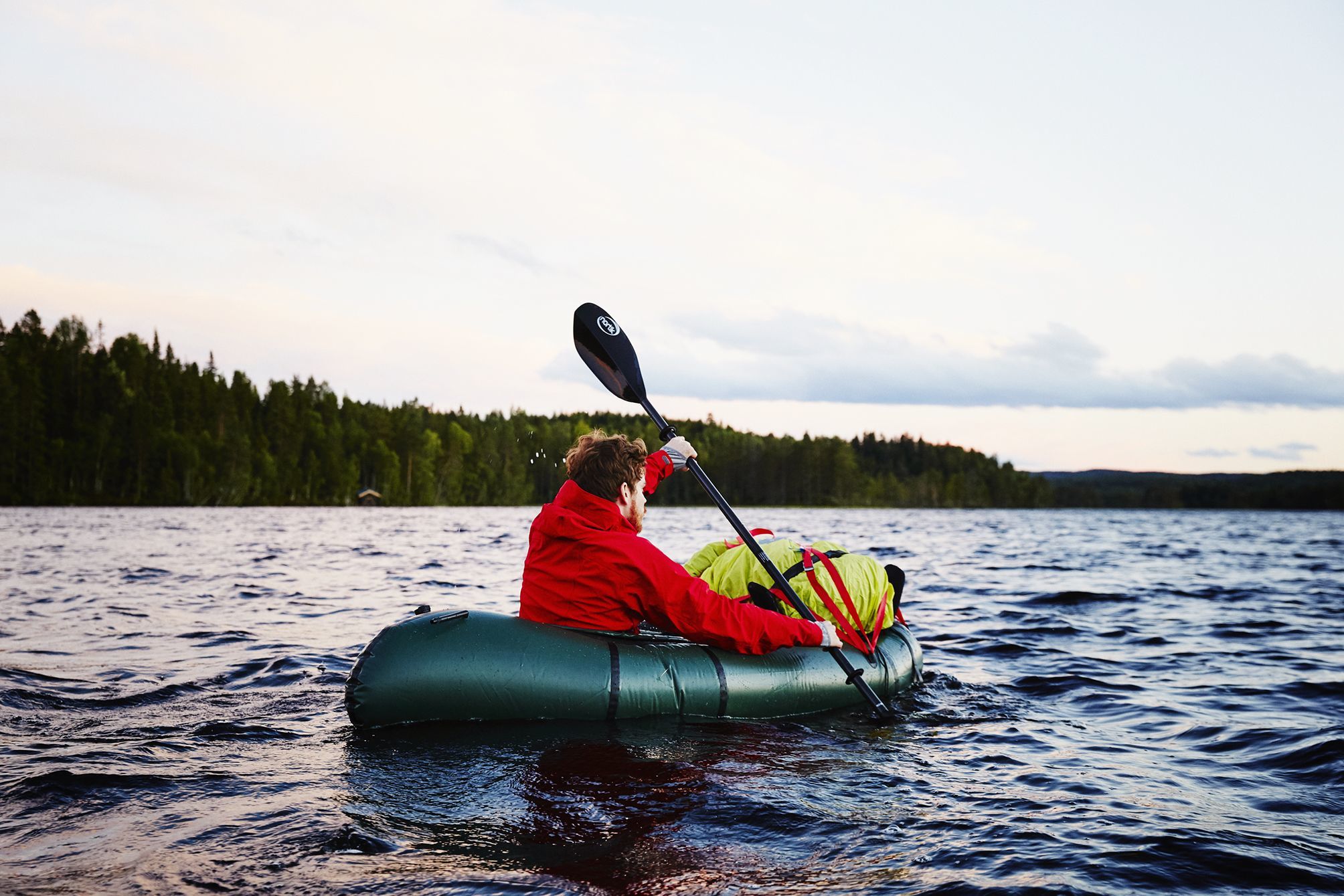 Young man paddling his packraft across a lake at dusk in the district near Oslo.