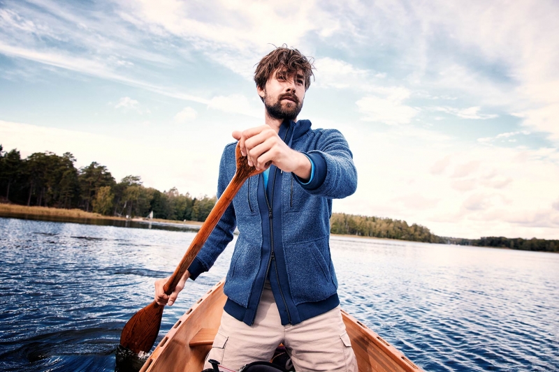 Young fair fashion model kneeing in his canoe in a lake, juxtaposed in front of the sky. Sustainable Outdoor Fashion Photography: Natural Light, Movement, and Ethics Aligned