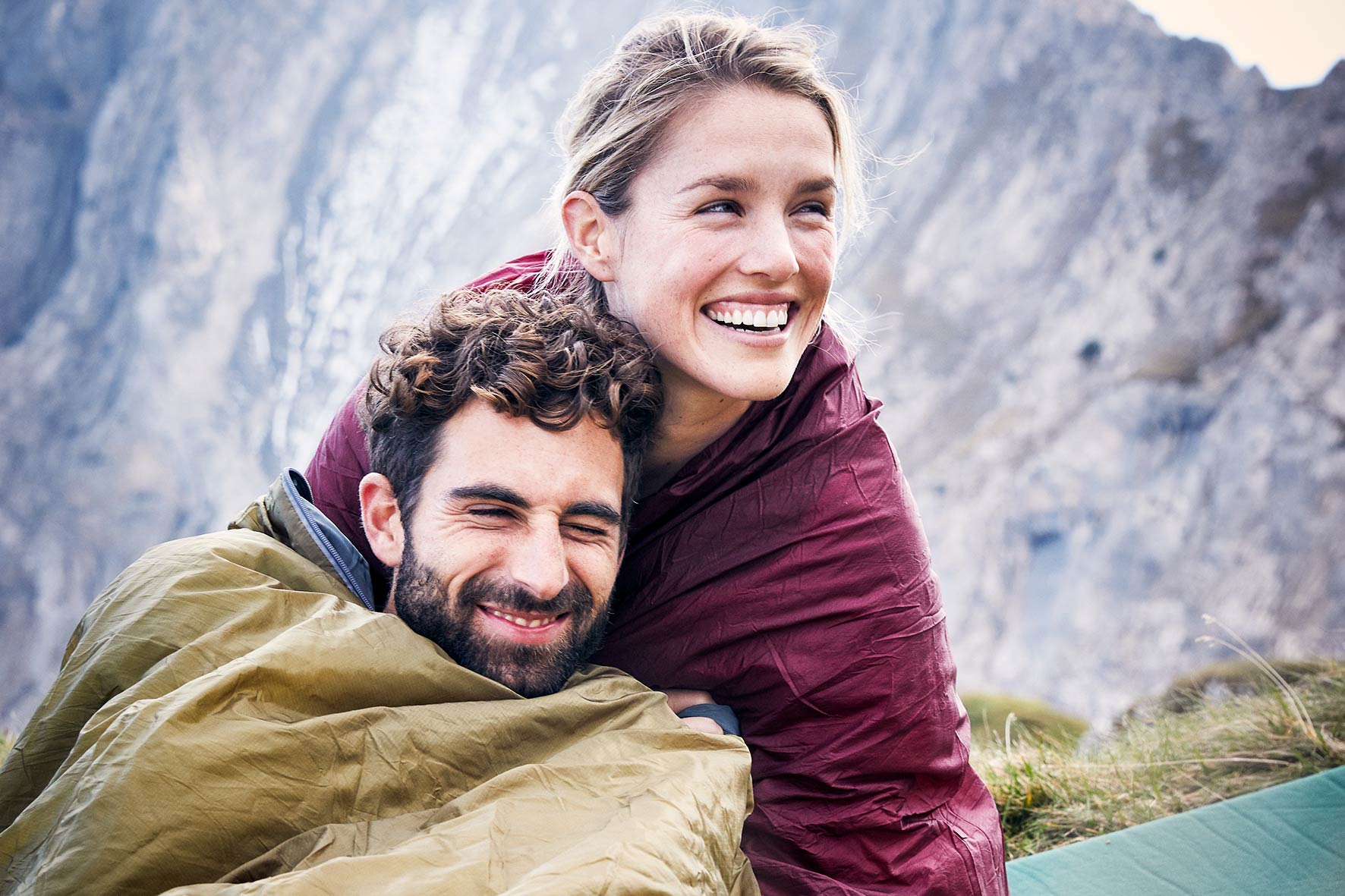 Man and woman cuddling in their sleepingbags during a sports photo shoot in the austrian alps and laughing.