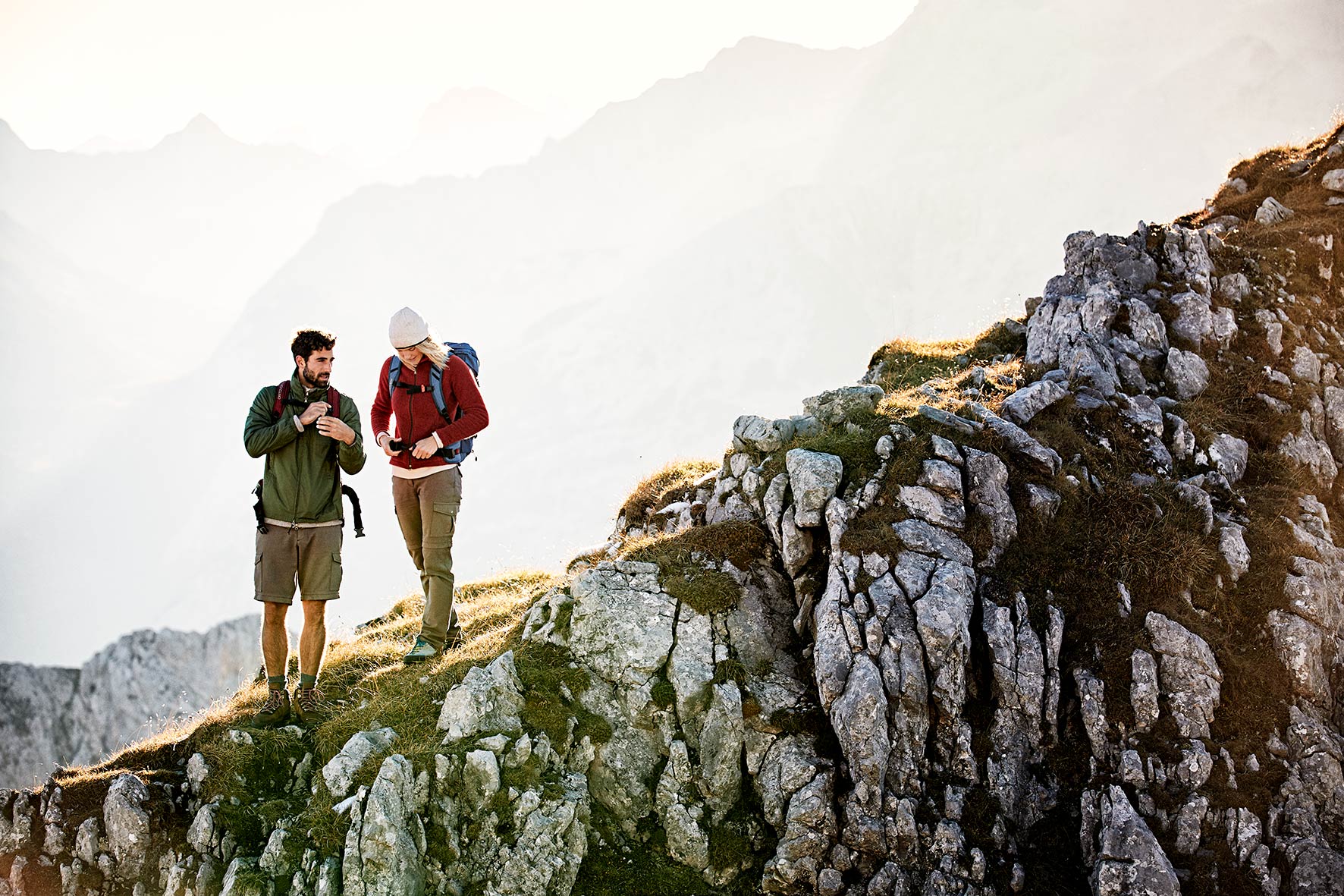 Couple trekking ontop of the Karwendel Mountain range, tightening their backpacks after a short break.