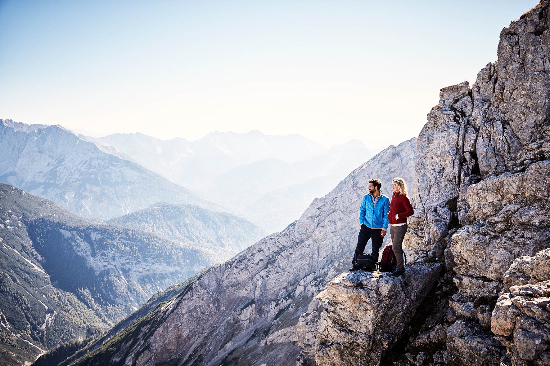 Sustainable fashion campaign wide shot of a couple standing on the ledge of a mountain face in the bavarian alps