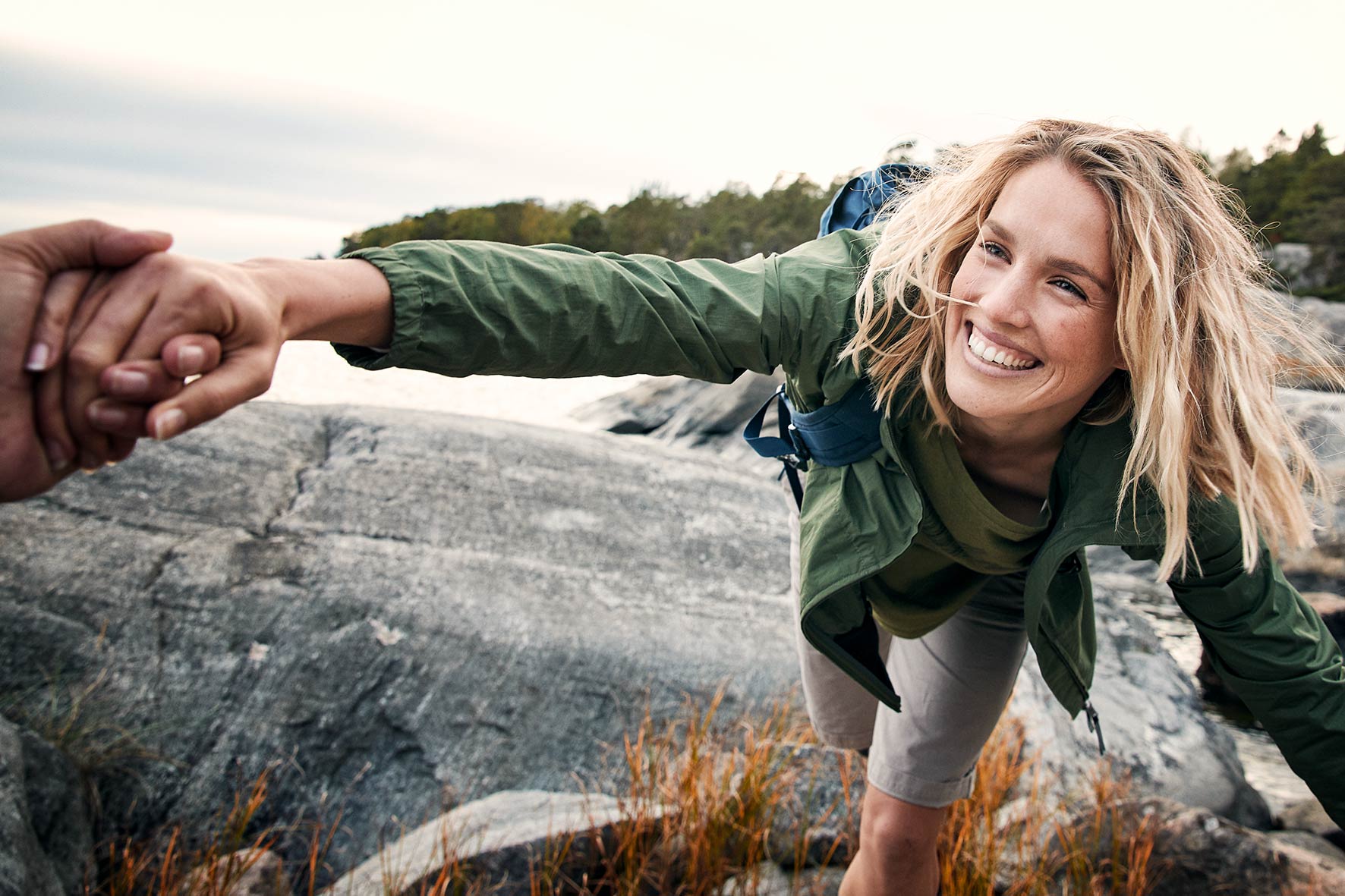 Girl jumping over the rocks by the sea near Stockholm is given a helping hand by a man outside the frame.