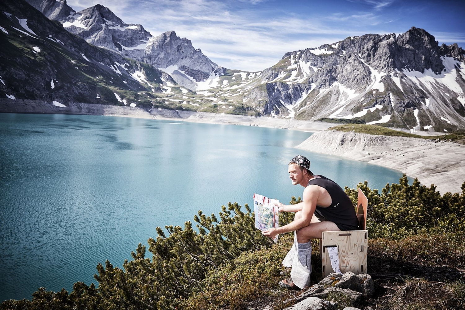 aerial photo of a man sitting on a toilet with a view of the luenersee and the mountains in the background