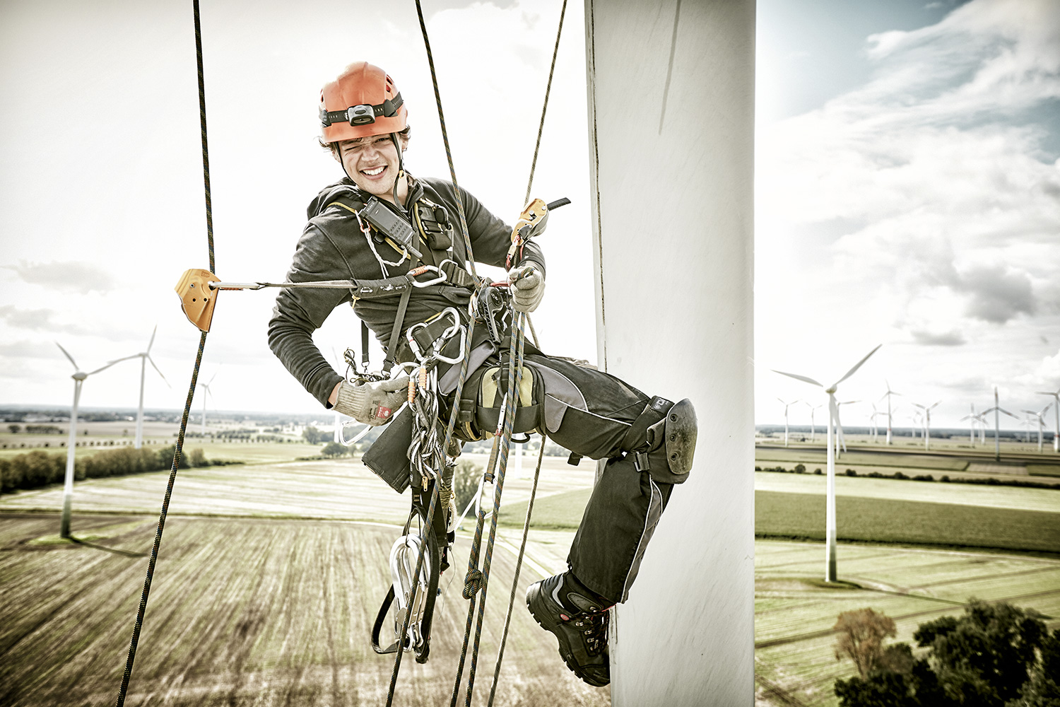 Wind Turbine Engineer grins into the camera while abseiling down a rotor blade