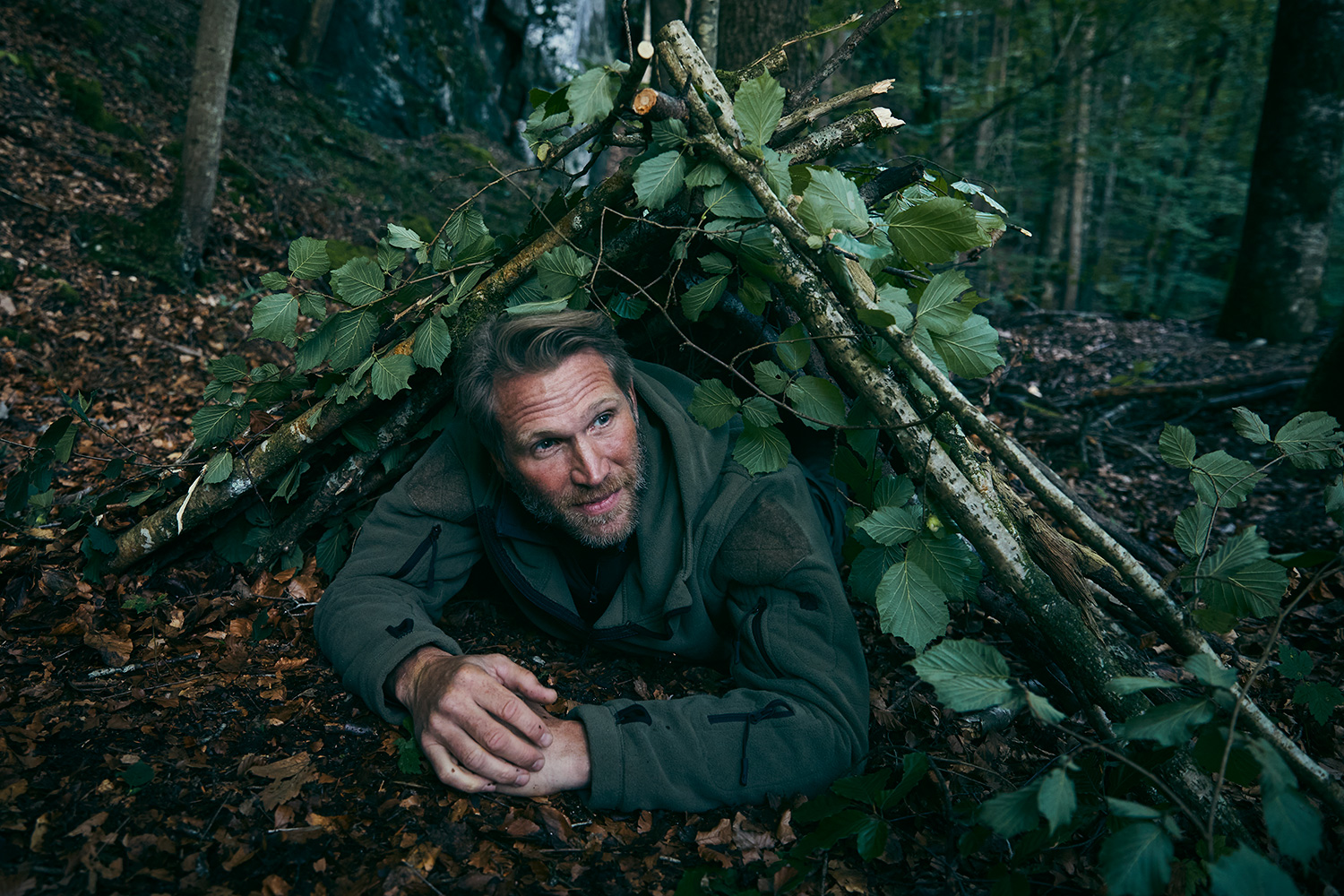 Man testing his night shelter in the woods on a survival camp