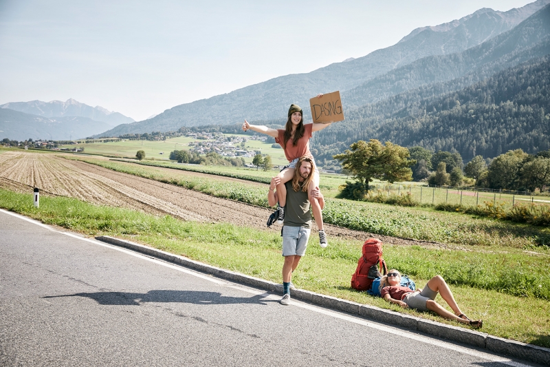 Three friends hitchhiking at the side of the road towards Dasing with their TATONKA backpacks