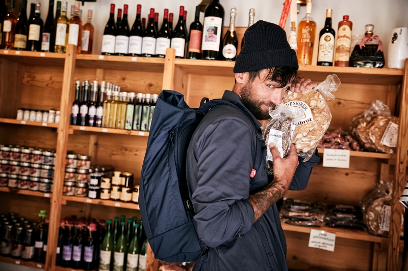 Man buying food in a gourmet shop wearing a backpack by TATONKA