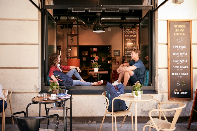 Boy and girl sitting with their TATONKA backpacks in the window of a cafe in Innsbruck
