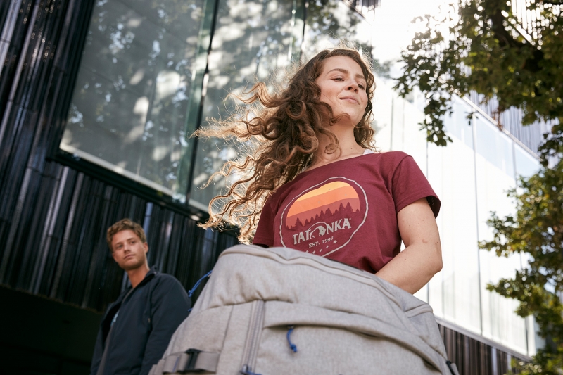 Woman shaking her hair with a TATONKA bag infront of her, and a boy watching her behind
