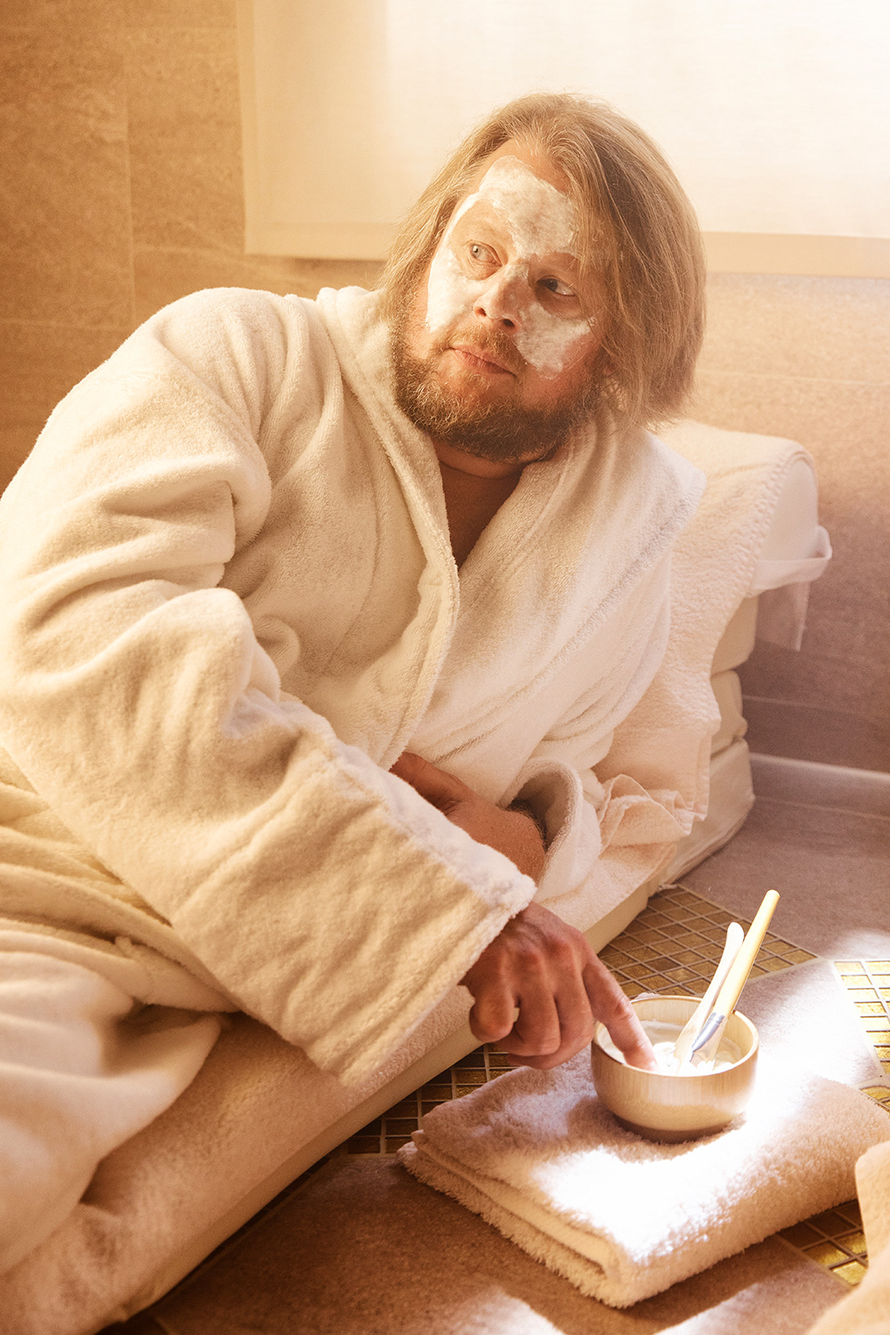 Man lying on a massage table in a bath robe with a face mask on