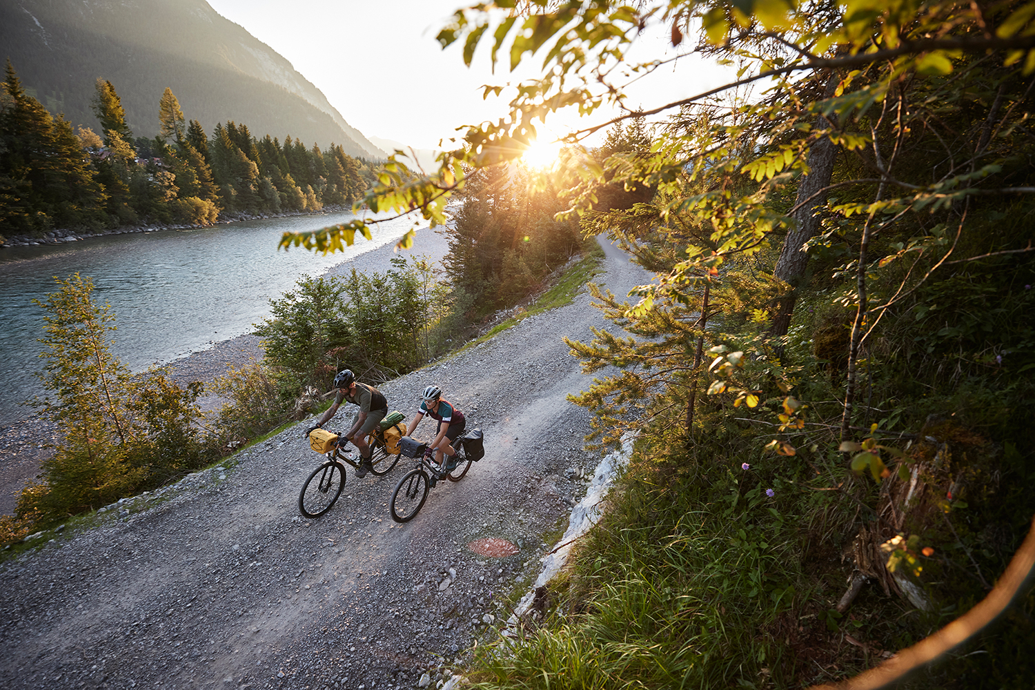 Couple cycling along a gravel road next to a river at sunrise