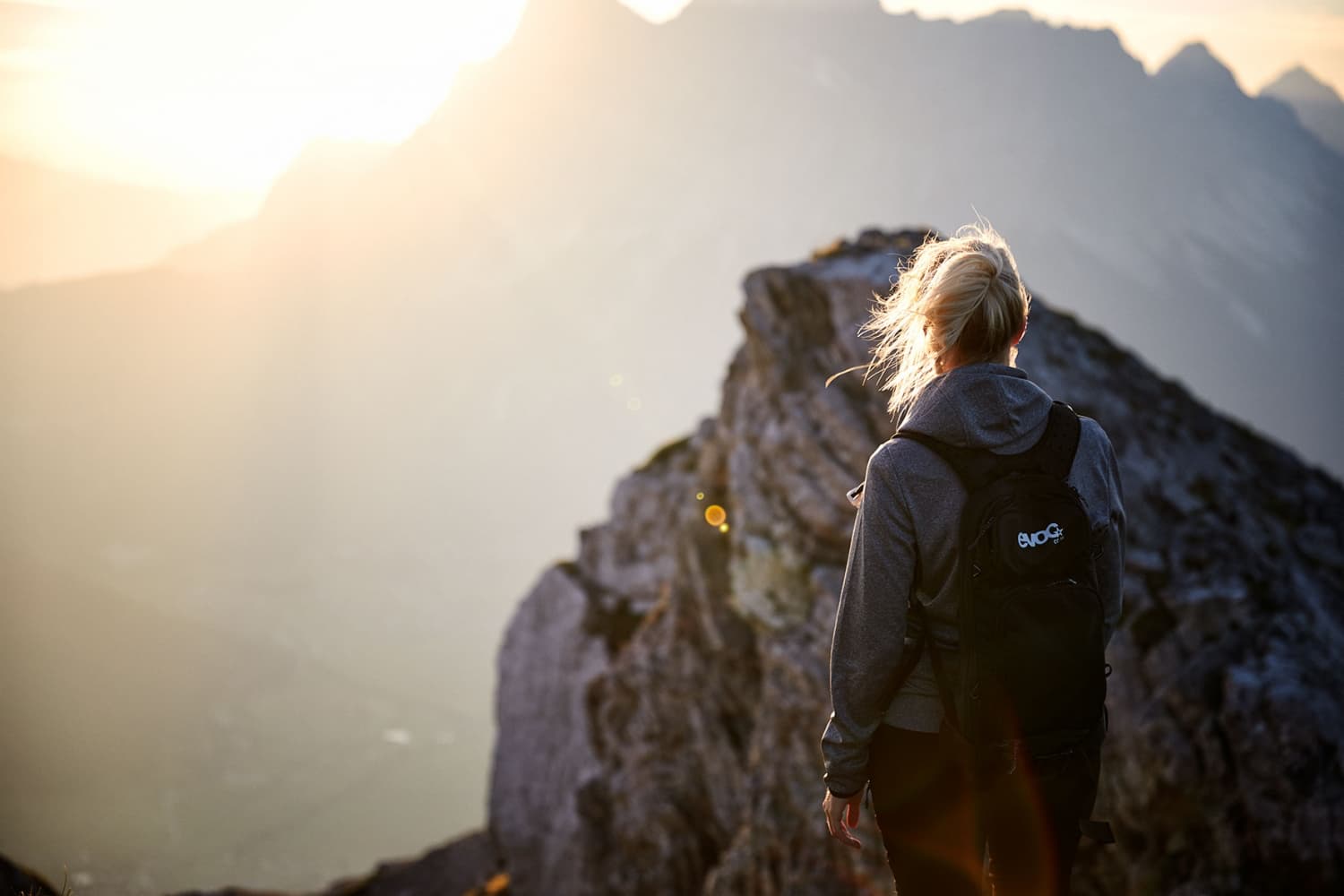 Woman looking into the ssunset ontop of a mountain wearing an evoc packpack