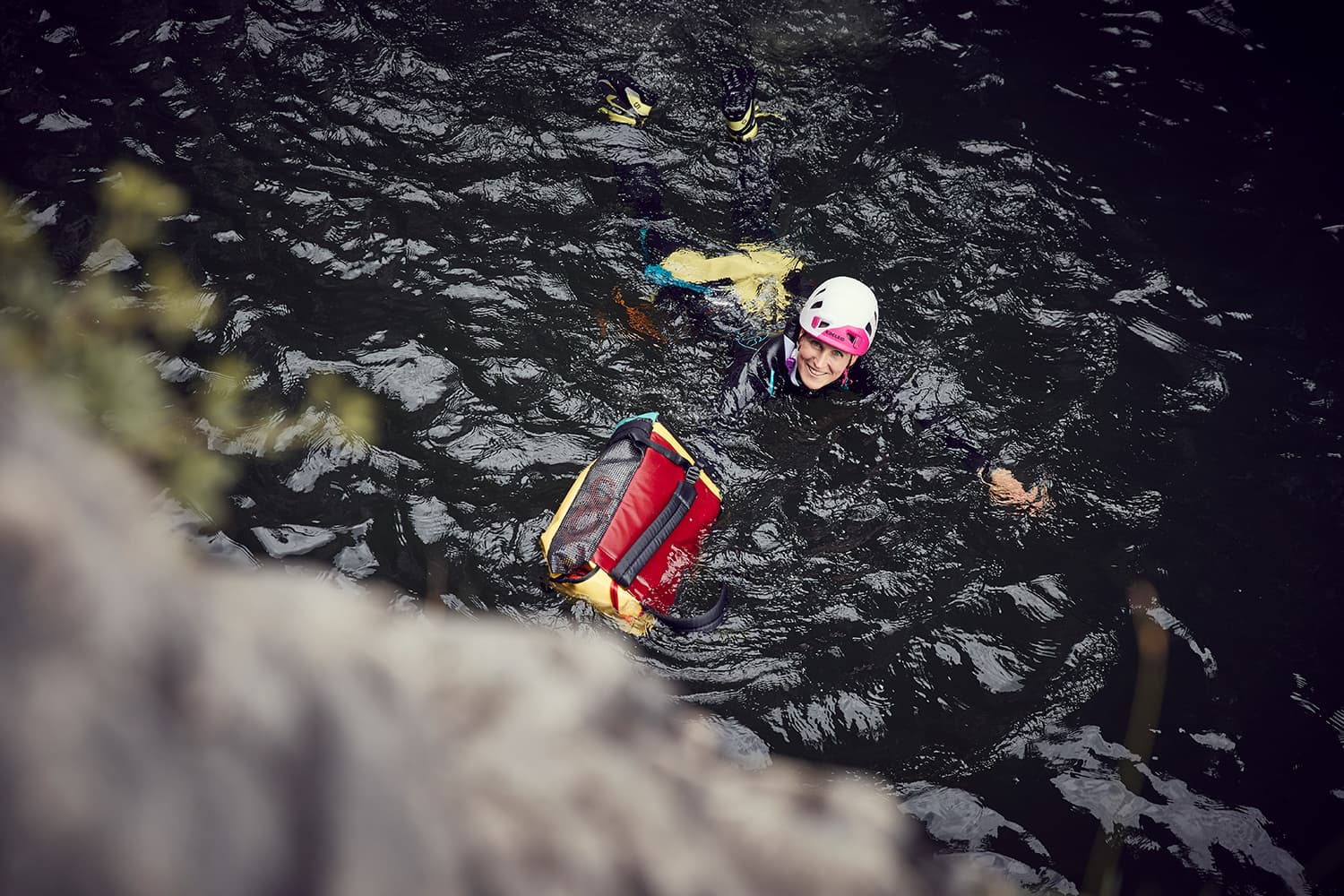 Stunt woman Kim swimming through a black pool pushing a bag and wearing a helmet while canyoning