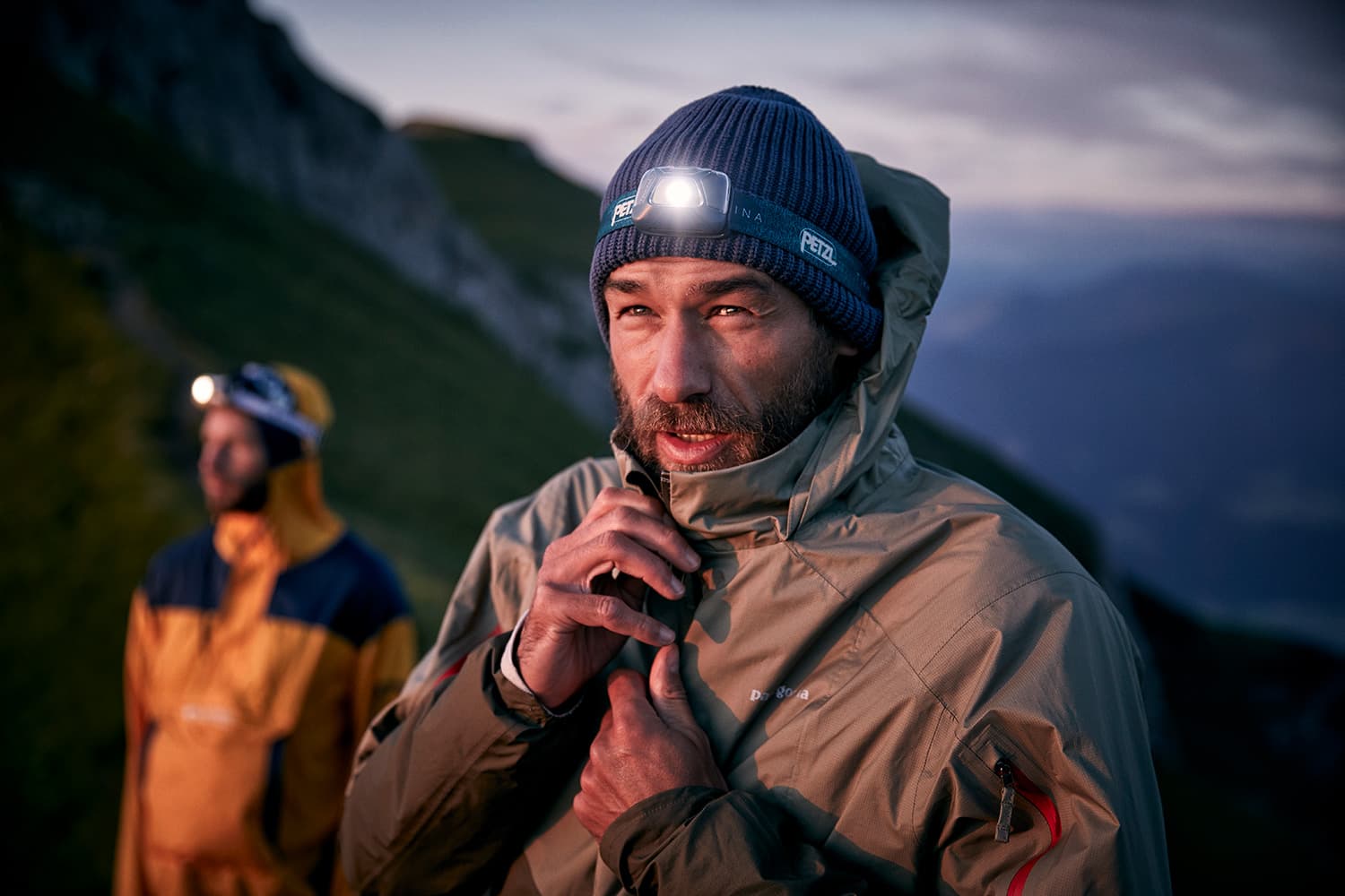 Portrait of a man closing his jacket while wearing a petzl headtorch while on a trailrun in the sunrises