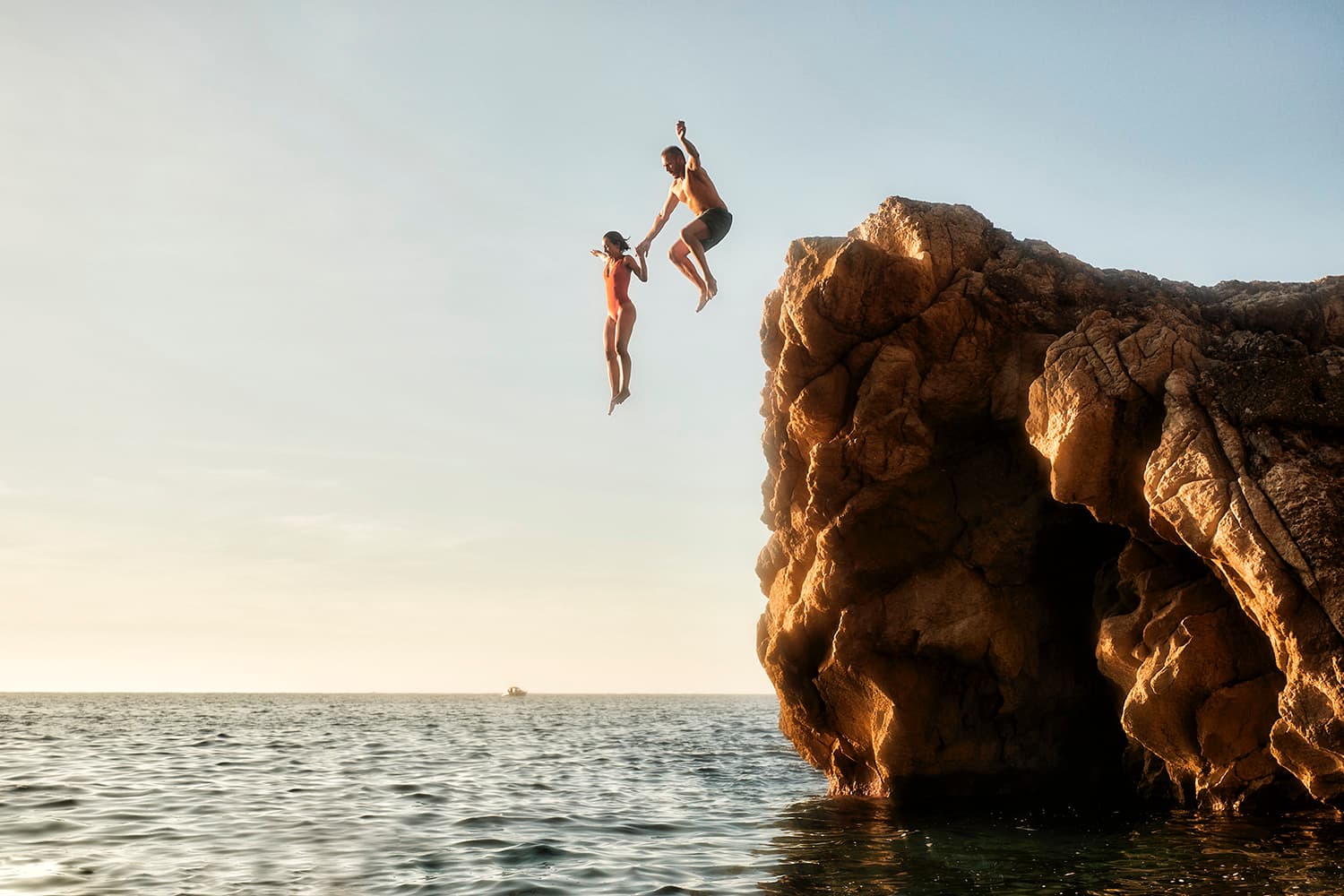 Couple jumping off a cliff into the sunset on Mallorca
