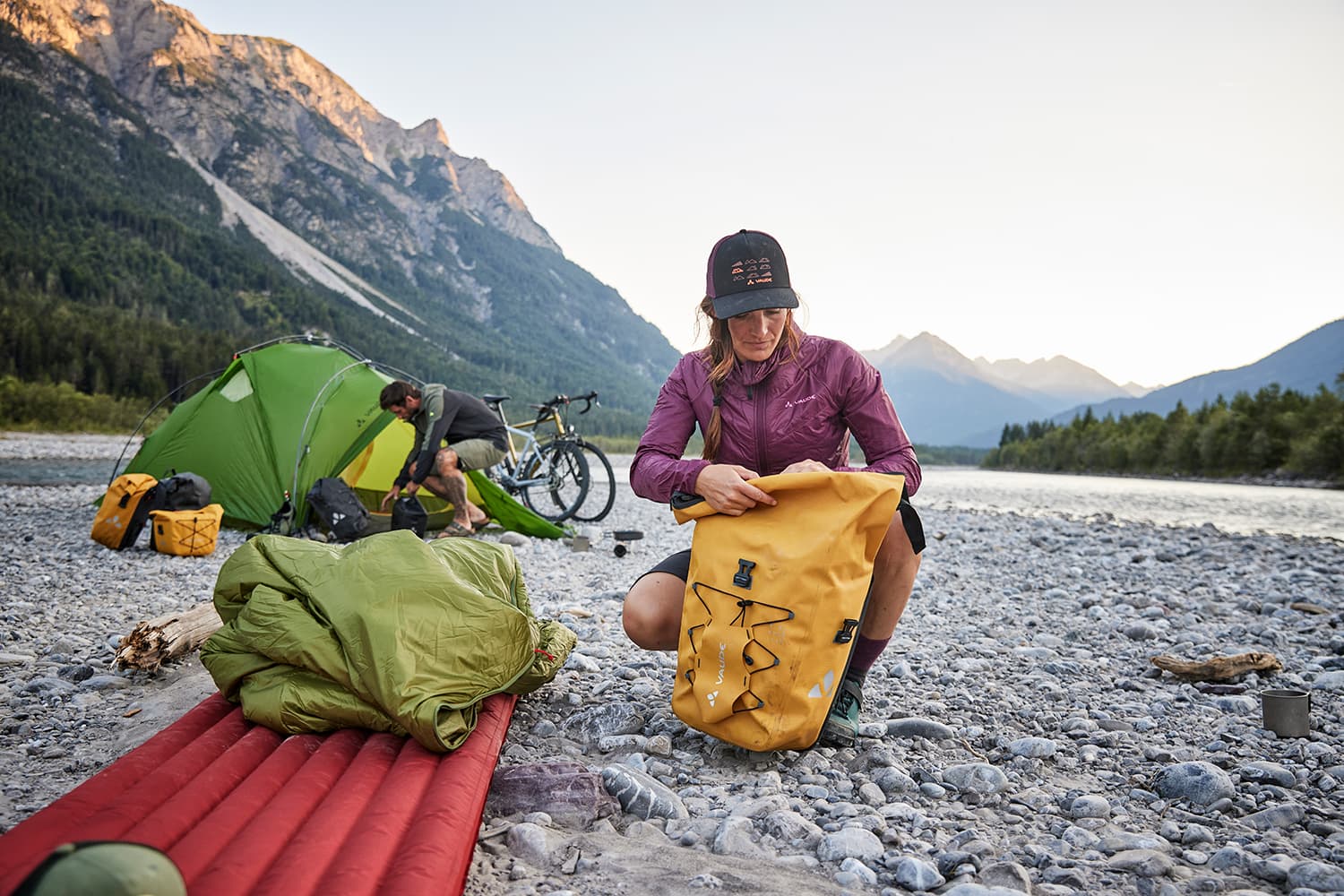 Woman cyclist setting up camp by the river and unpacking her cycle bags