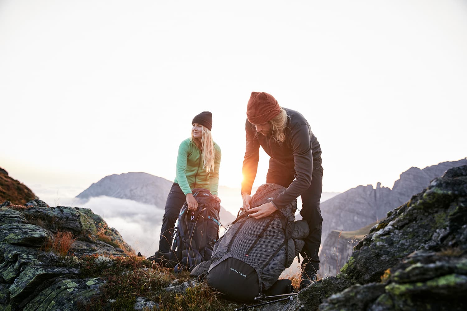 A couple taking off their TATONKA backpacks at sunrise ontop of Axamer Lizum in Austria