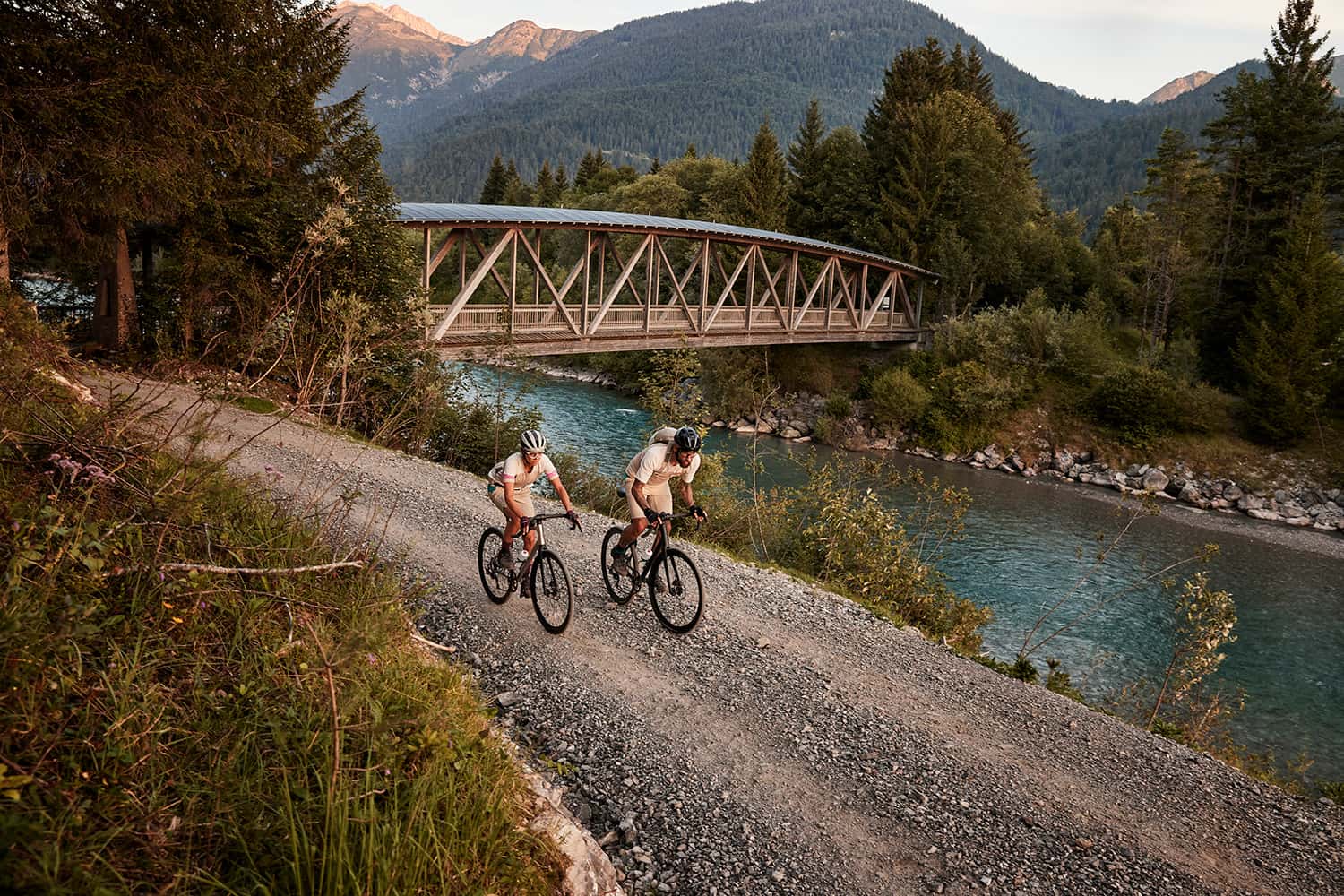 Couple cycling along a gravel road by a river before sunrise